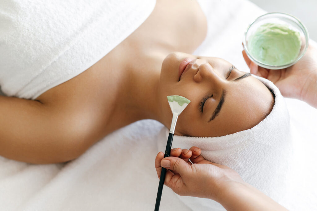 Woman receiving a facial treatment with green mask applied, emphasizing skincare and anti-aging benefits at Physician Aesthetic Institute.