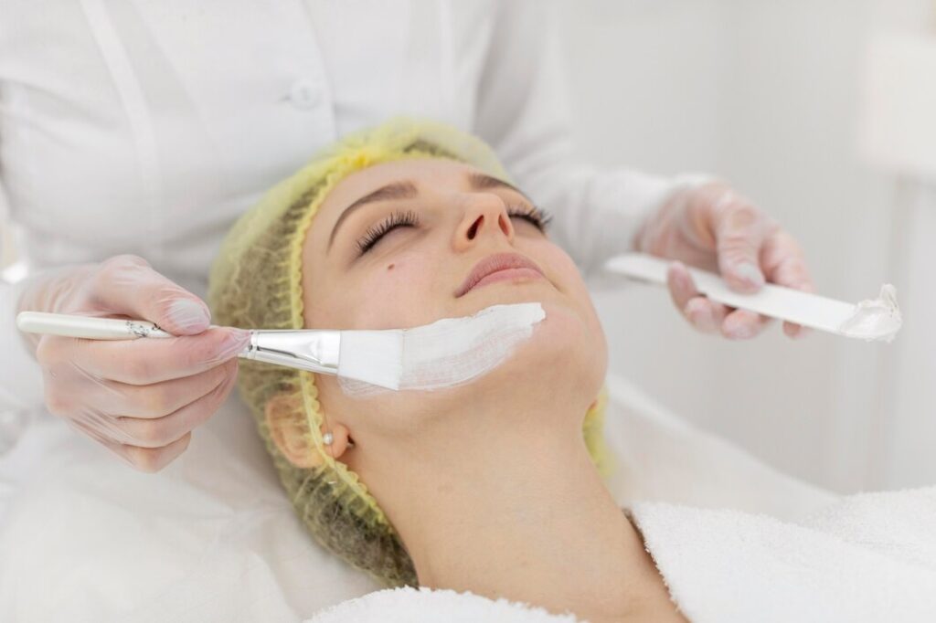 Woman receiving a chemical peel treatment, with a clinician applying a white chemical solution to her face, highlighting skincare rejuvenation and exfoliation benefits.