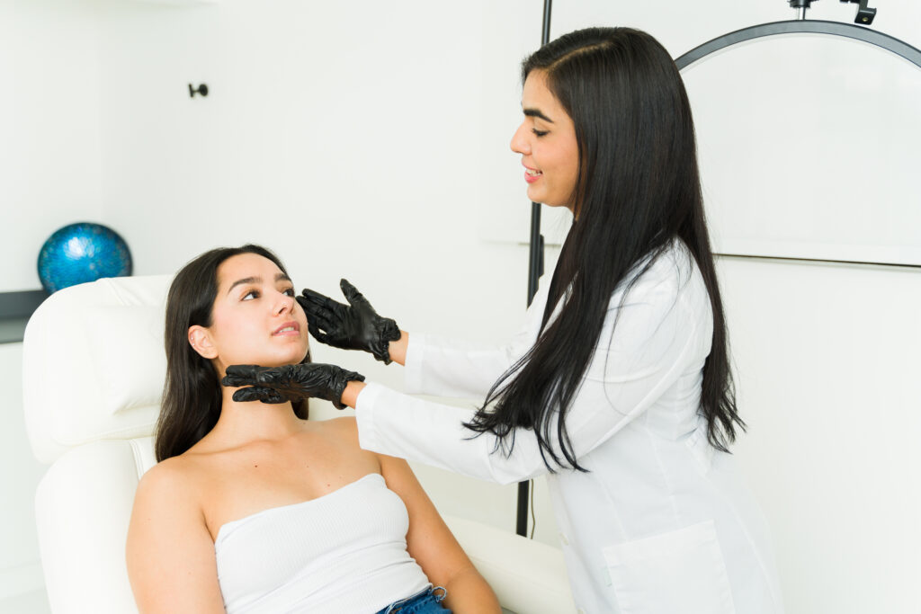 Female aesthetician in white coat performing skin consultation on female patient in treatment chair, highlighting microneedling and chemical peel options for skincare.